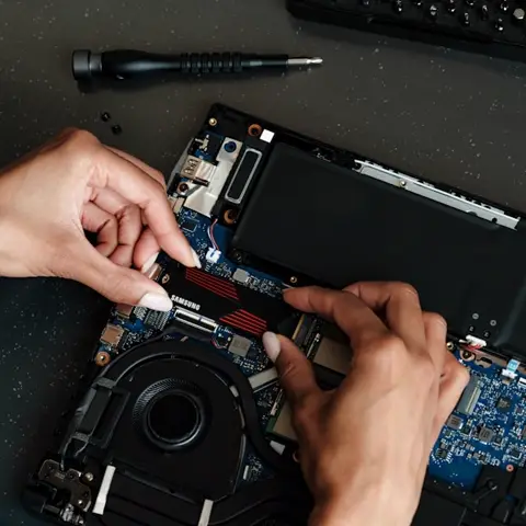 Hands upgrading a laptop SSD with a screwdriver — computer technician work